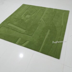 May include: A green wool rug with a geometric pattern. The rug has a raised texture and is made of high-quality materials.