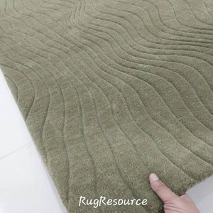 May include: A close-up of a green rug with a wavy pattern. The rug is made of a soft, plush material and has a subtle sheen. The text "RugResource" is visible in the lower right corner of the image.