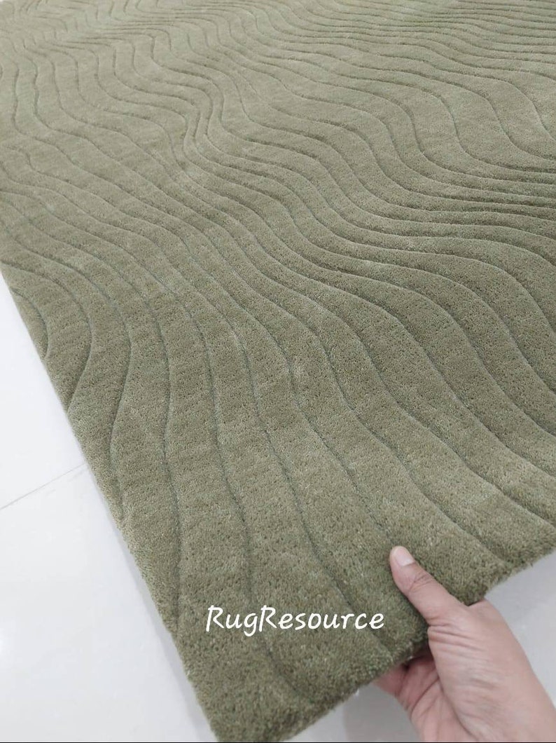 May include: A close-up of a green rug with a wavy pattern. The rug is made of a soft, plush material and has a subtle sheen. The text "RugResource" is visible in the lower right corner of the image.