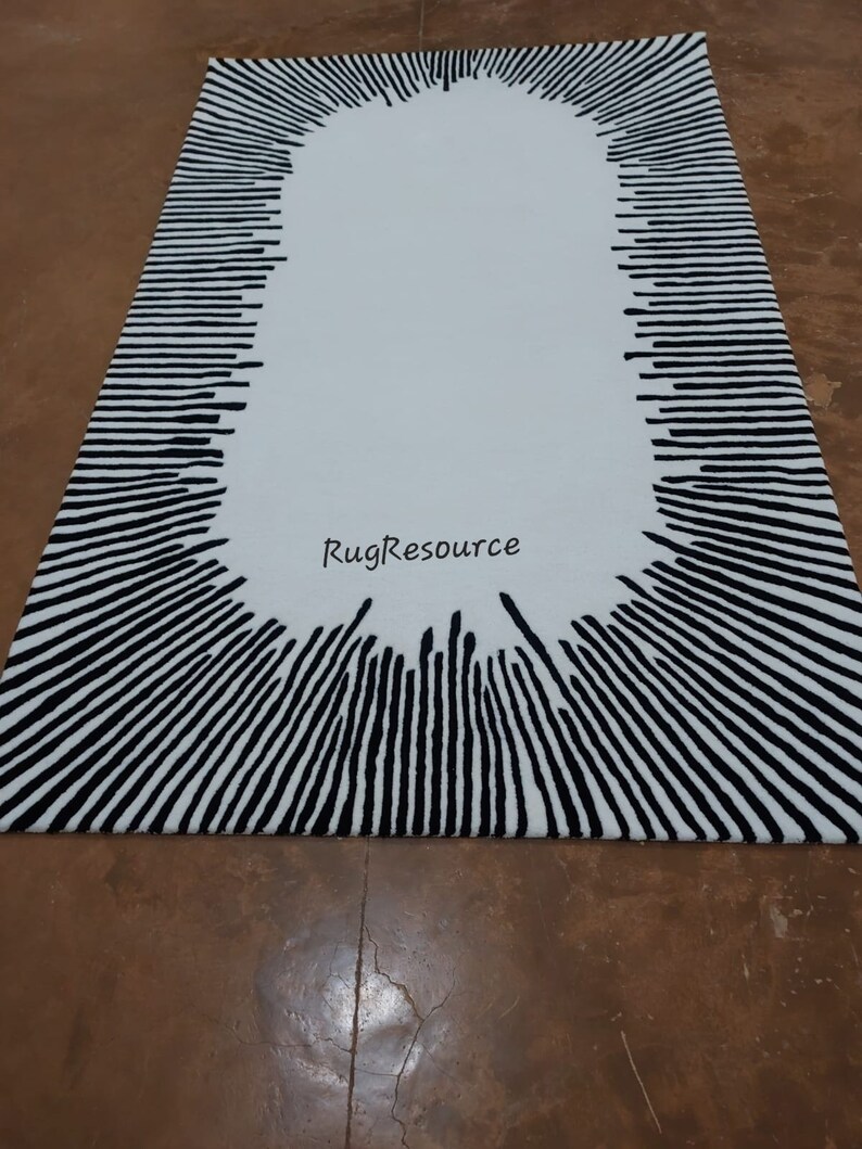 May include: A white oval rug with a black and white striped border. The stripes are arranged in a radial pattern, creating a sunburst effect. The rug has the text "RugResource" in the center.