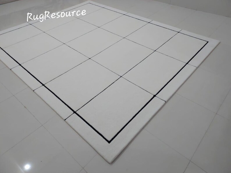 Pu&ograve; includere: Un tappeto bianco con un motivo a griglia, con linee nere che creano un design geometrico. Il tappeto ha un bordo nero e il testo "RugResource" nell'angolo in alto a sinistra.