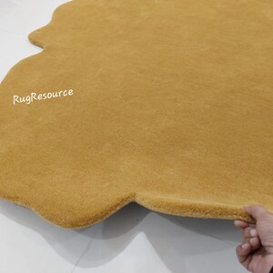 May include: A mustard yellow, fluffy, cloud-shaped rug with a slightly irregular shape. The rug is made of a soft, plush material and has a subtle sheen. The text "RugResource" is visible in the upper left corner of the rug.