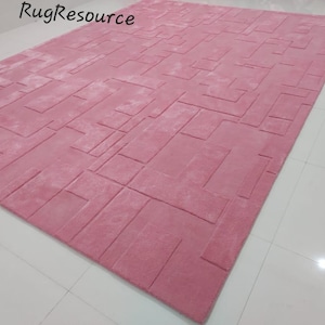 May include: A pink area rug with a geometric pattern. The rug has a raised texture and is made of soft, plush material.