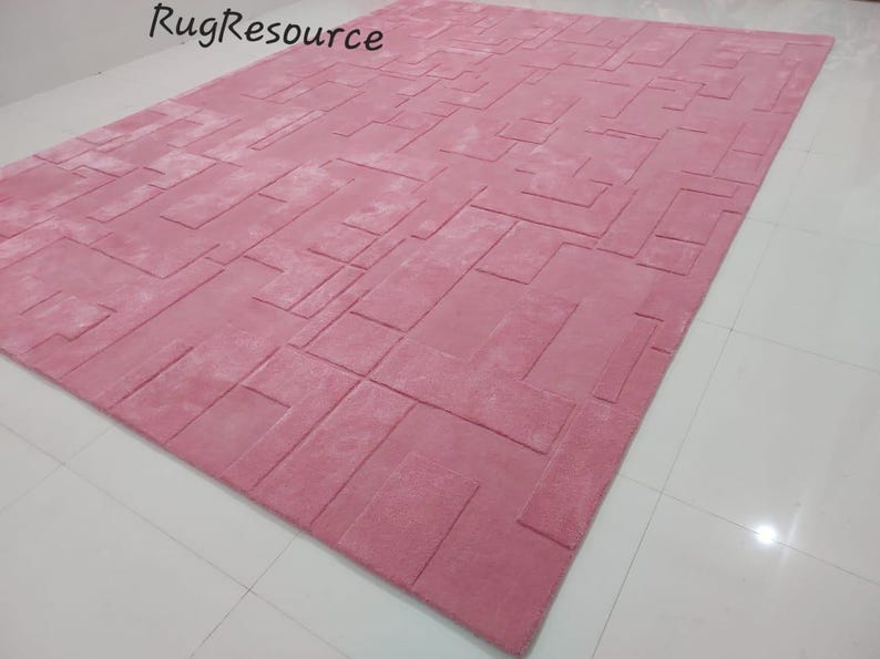 May include: A pink area rug with a geometric pattern. The rug has a raised texture and is made of soft, plush material.