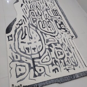 May include: A white and black abstract rug with a unique design. The rug has a fringe border and the text "RugResource" is printed on the bottom right corner.