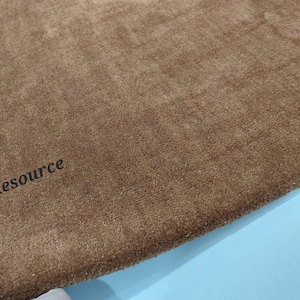 K&ouml;nnte beinhalten: Ein rechteckiger brauner Teppich mit einer dichten Kurzflor-Textur. Die Oberfl&auml;che weist subtile Farbnuancen in den Fasern auf. Der Text "RugResource" ist in schwarzen, serifenlosen Buchstaben in der unteren linken Ecke des Teppichs aufgedruckt.