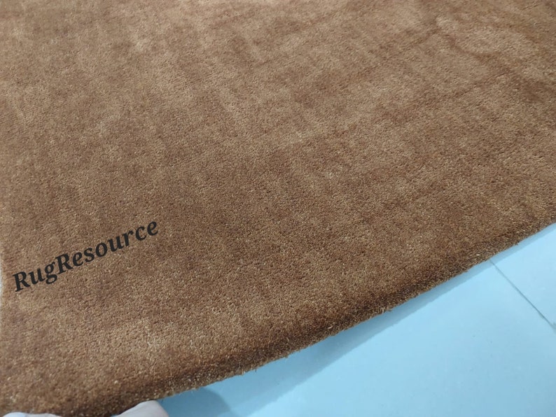 K&ouml;nnte beinhalten: Ein rechteckiger brauner Teppich mit einer dichten Kurzflor-Textur. Die Oberfl&auml;che weist subtile Farbnuancen in den Fasern auf. Der Text "RugResource" ist in schwarzen, serifenlosen Buchstaben in der unteren linken Ecke des Teppichs aufgedruckt.