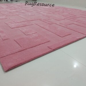 May include: A pink area rug with a geometric pattern. The rug has a raised texture and a subtle sheen.