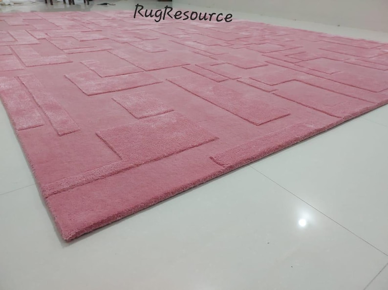 May include: A pink area rug with a geometric pattern. The rug has a raised texture and a subtle sheen.