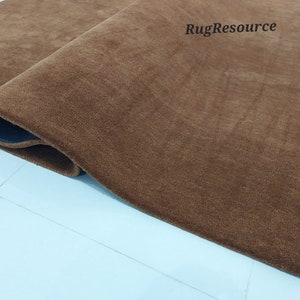 May include: Close-up of a brown, plush rug with a slightly darker brown border. The rug is rolled up and the edge is visible. The text "RugResource" is visible in the upper right corner of the image.