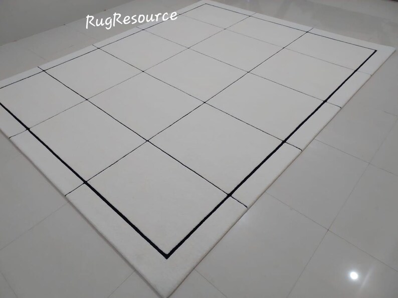 Pu&ograve; includere: Un tappeto rettangolare bianco con un motivo a griglia creato da linee nere. Il tappeto ha un bordo nero ed &egrave; posizionato su un pavimento piastrellato bianco. Il testo "RugResource" &egrave; visibile nell'angolo in alto a sinistra.