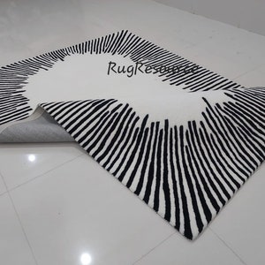 May include: A white and black striped rug with a circular design in the center. The rug is rolled up and the underside is visible.