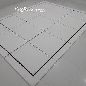 Pu&ograve; includere: Un tappeto rettangolare bianco con un motivo a griglia, delineato da un bordo nero. Il design pulito e il colore neutro del tappeto lo rendono adatto a una variet&agrave; di stili di interni. Il testo "RugResource" &egrave; visibile.