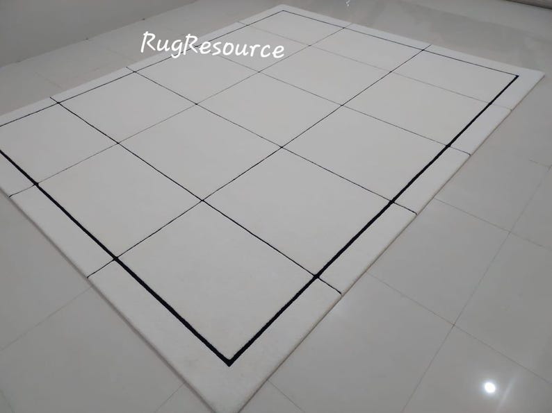 Pu&ograve; includere: Un tappeto rettangolare bianco con un motivo a griglia, delineato da un bordo nero. Il design pulito e il colore neutro del tappeto lo rendono adatto a una variet&agrave; di stili di interni. Il testo "RugResource" &egrave; visibile.