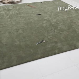 May include: A large, olive green rug with a soft, textured surface. The rug is rectangular and covers most of the floor. Several small decorative items are scattered on the rug. The words "RugResource" are visible in the top right corner.