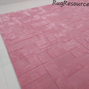 May include: A pink area rug with a geometric pattern. The rug has a textured surface and is made of a soft material.