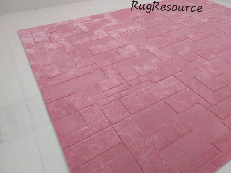 May include: A pink area rug with a geometric pattern. The rug has a textured surface and is made of a soft material.