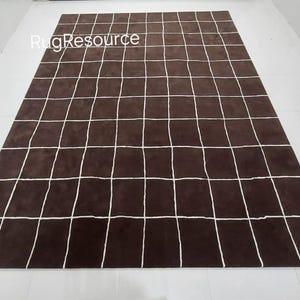 Peut inclure: Un tapis brun avec un motif en grille blanche. RugResource est imprimé dans le coin supérieur gauche.