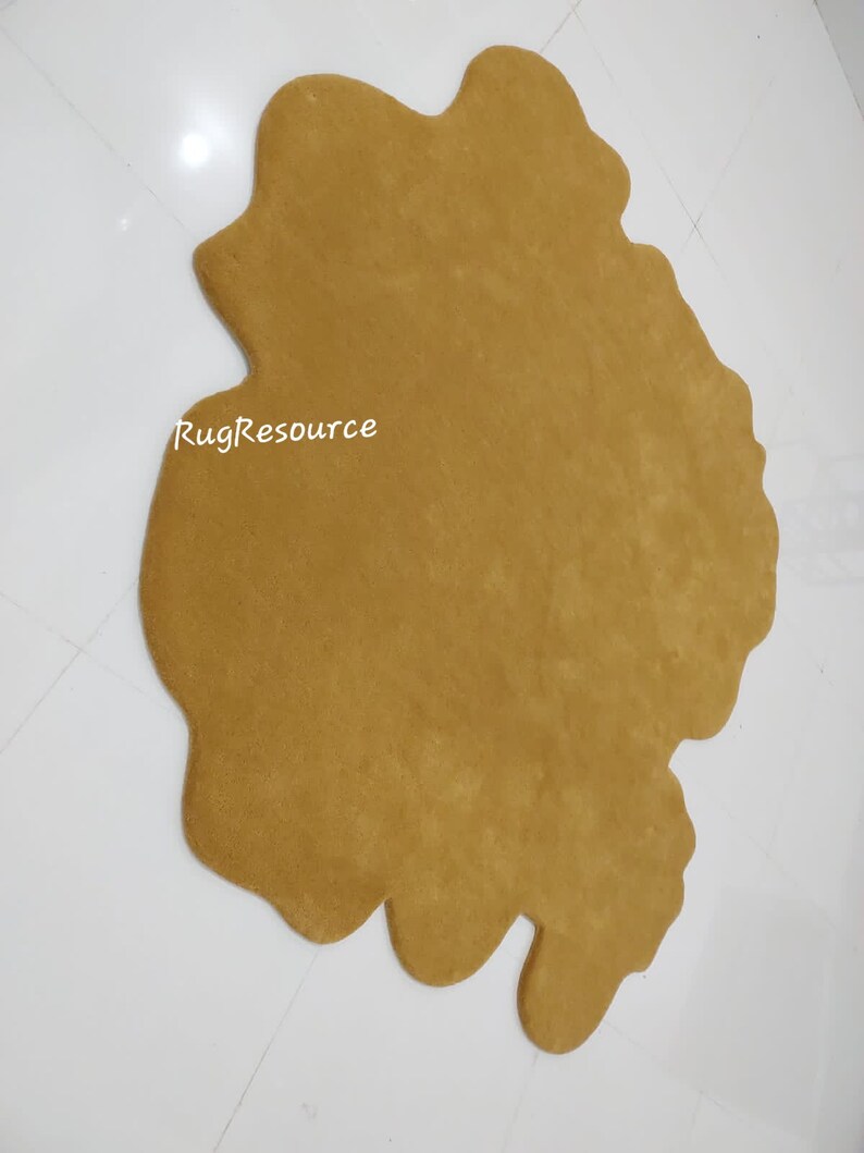 May include: A large, brown, irregularly shaped rug with a soft, fuzzy texture. The rug is made of a plush material and has a unique, organic shape. The text "RugResource" is visible in the lower left corner of the rug.