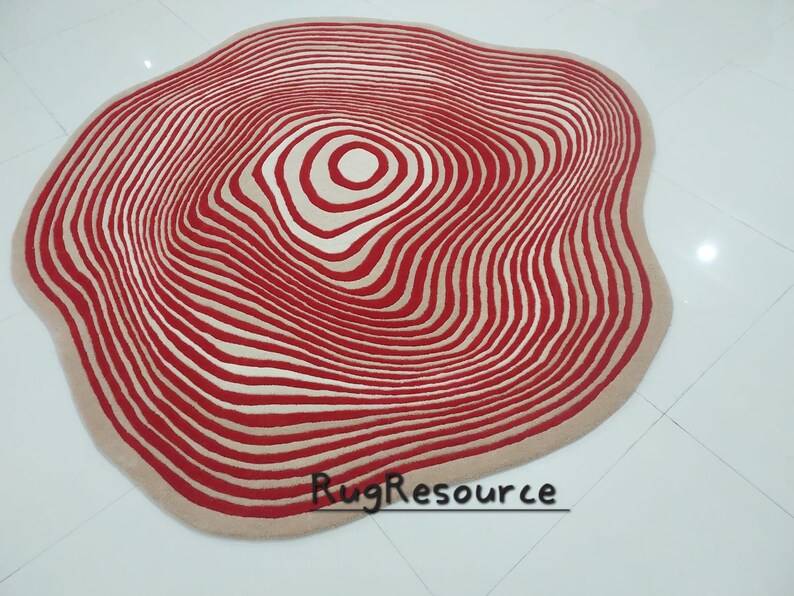 May include: A large, round, cream-colored rug with a red and cream concentric circle pattern. The rug has a wavy, organic shape.