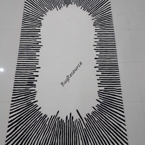 May include: A white rug with a black oval design in the center. The oval is surrounded by black lines radiating outwards.