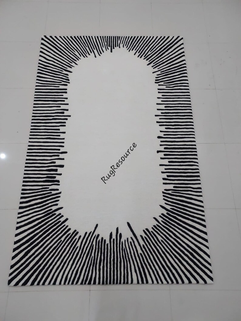 May include: A white rug with a black oval design in the center. The oval is surrounded by black lines radiating outwards.