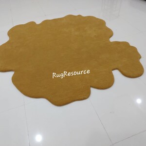 May include: A large, mustard yellow, fluffy, irregularly shaped rug. The rug is made of a soft, plush material and has a unique, organic shape.