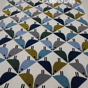 May include: A white rug with a geometric pattern of blue, green, and yellow birds. The rug has a modern design and is perfect for a living room or bedroom.