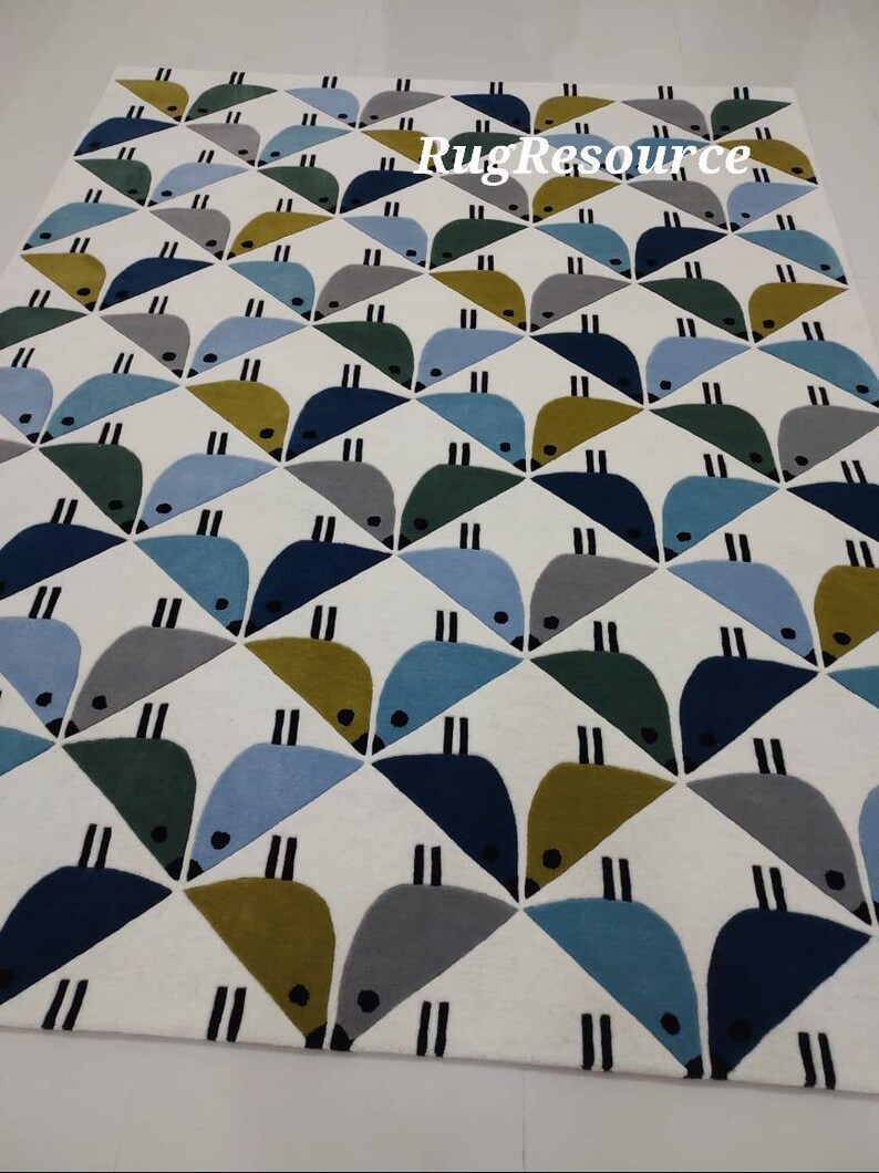 May include: A white rug with a geometric pattern of blue, green, and yellow birds. The rug has a modern design and is perfect for a living room or bedroom.