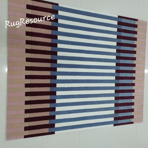 May include: A striped rug with pink, burgundy, blue, and white stripes. The rug has a modern geometric design.