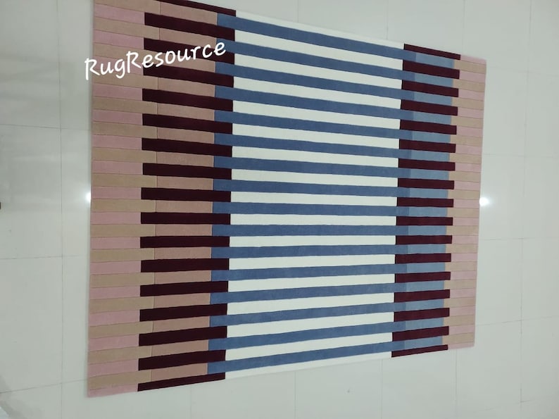 May include: A striped rug with pink, burgundy, blue, and white stripes. The rug has a modern geometric design.