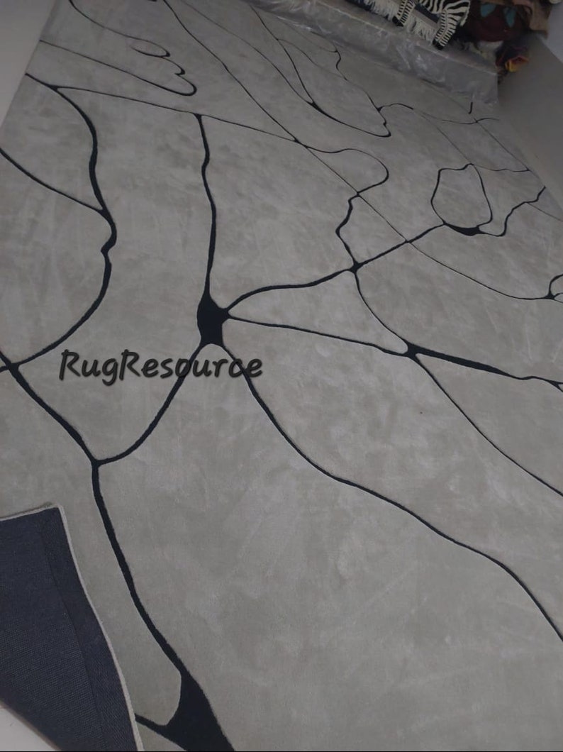 Puede incluir: Una alfombra gris y negra con un dise&ntilde;o abstracto moderno. La alfombra presenta una red de l&iacute;neas negras que se asemejan a venas o ramas, creando un aspecto &uacute;nico y contempor&aacute;neo.