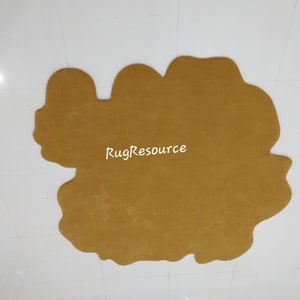 May include: A large, mustard yellow, irregularly shaped rug with a slightly fuzzy texture. The rug is on a white tiled floor. The text "RugResource" is printed in white on the rug.