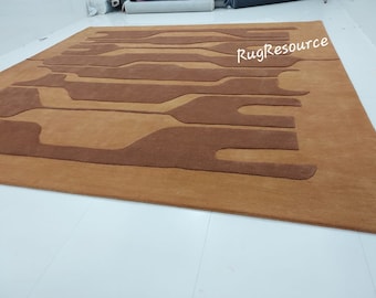 May include: A brown and tan abstract area rug with a modern design. The rug has a raised texture and a subtle sheen. The text "RugResource" is visible in the upper right corner of the rug.