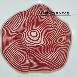May include: A red and cream colored rug with a circular design that resembles tree rings. The rug has a wavy edge.