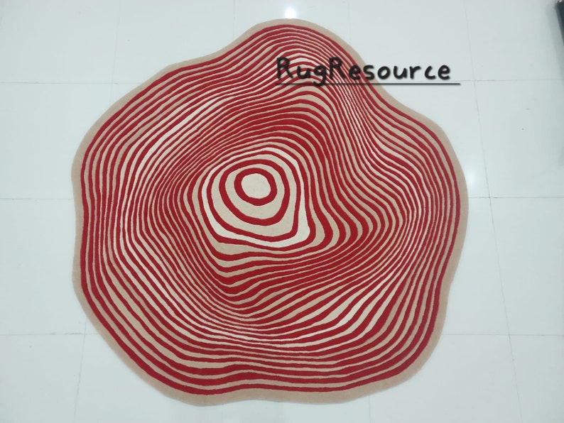 May include: A red and cream colored rug with a circular design that resembles tree rings. The rug has a wavy edge.