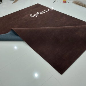 May include: A brown rug with a gray backing. The rug is folded in half and the backing is visible. The rug is on a white tiled floor.