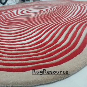 May include: A red and white striped rug with a wavy, organic shape. The rug has a concentric circle pattern in the center.