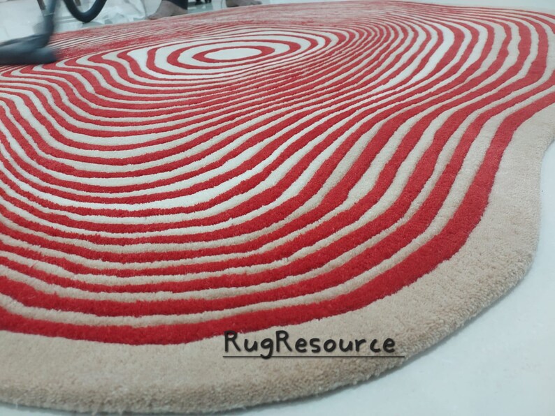 May include: A red and white striped rug with a wavy, organic shape. The rug has a concentric circle pattern in the center.