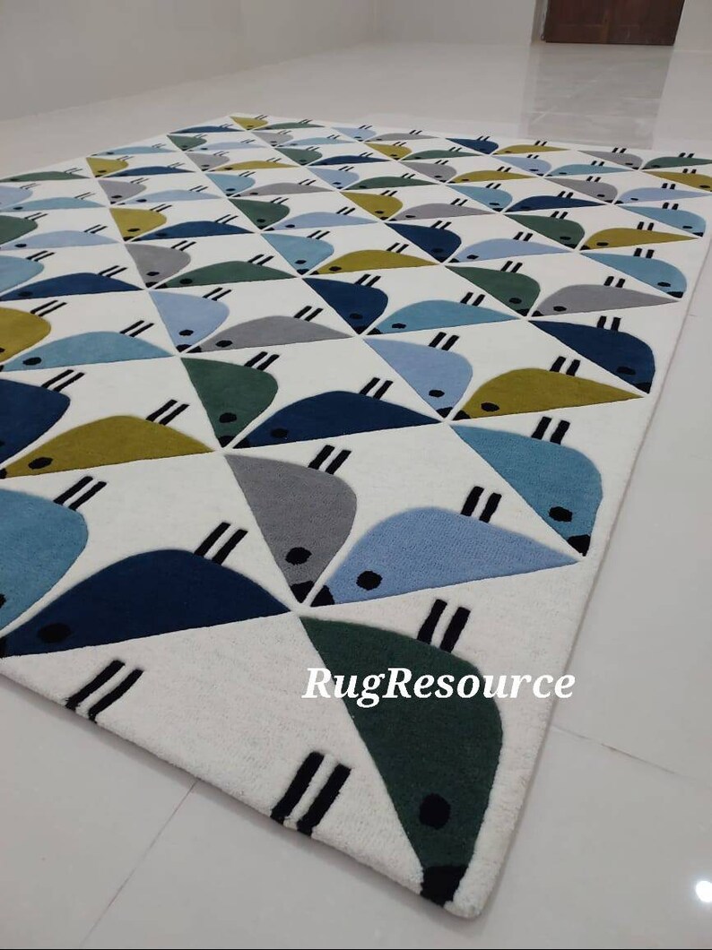 May include: A white rug with a geometric pattern of blue, green, and yellow birds. The rug has a white background with a black outline around the birds. The rug is made of a soft, plush material. The text "RugResource" is printed in the bottom right corner of the rug.