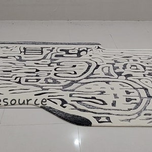 May include: Abstract black and white area rug with a unique, organic shape. The rug has a modern, contemporary design with a textured, woven surface.
