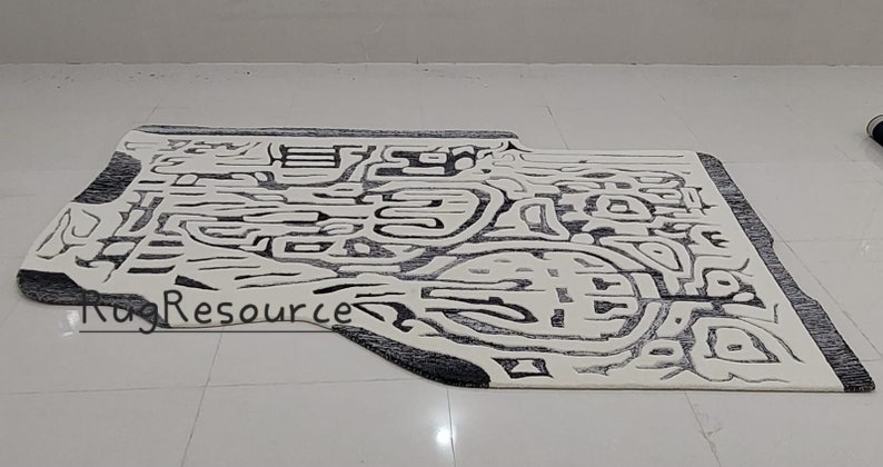 May include: Abstract black and white area rug with a unique, organic shape. The rug has a modern, contemporary design with a textured, woven surface.