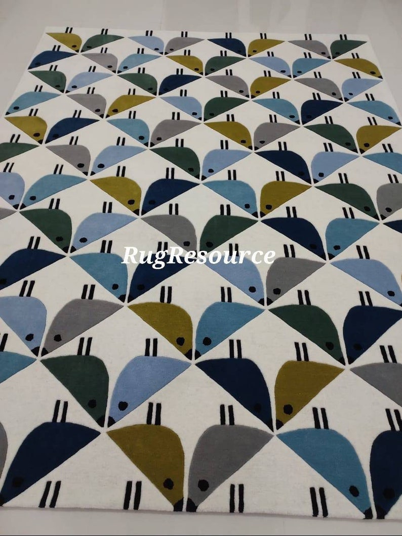 May include: A white rug with a geometric pattern of blue, green, gray, and yellow birds. The birds are arranged in a repeating pattern of triangles.