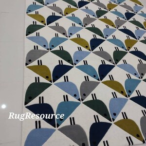 May include: A white rug with a geometric pattern of blue, green, gray, and yellow birds. The rug has a white background and the birds are arranged in a repeating pattern. The rug is made of wool and has a soft, plush texture. RugResource is printed in the bottom left corner of the rug.