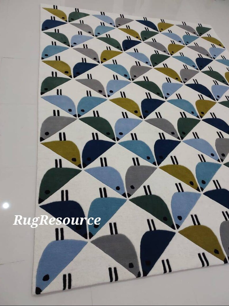 May include: A white rug with a geometric pattern of blue, green, gray, and yellow birds. The rug has a white background and the birds are arranged in a repeating pattern. The rug is made of wool and has a soft, plush texture. RugResource is printed in the bottom left corner of the rug.