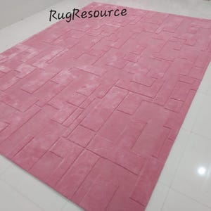 May include: A pink area rug with a geometric pattern. The rug has a soft, plush texture and is perfect for adding a touch of color and style to any room.