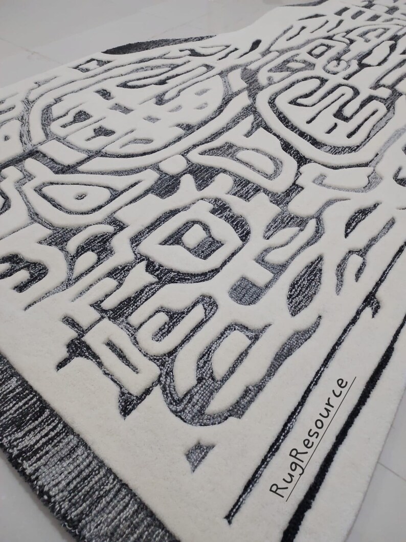 May include: A white rug with a black and gray abstract design. The design features a variety of shapes and lines, creating a modern and geometric look. The rug has a black border and the text "RugResource" is printed in the bottom right corner.