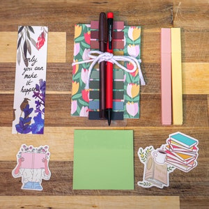 May include: A set of stationery supplies including two bookmarks, two highlighters, a set of sticky notes, a green notepad, and two stickers. One bookmark features a floral design and the text "only you can make it happen". One sticker features a person reading a book with flowers on top of the book. The other sticker features a stack of books with a cup of coffee and a plant.