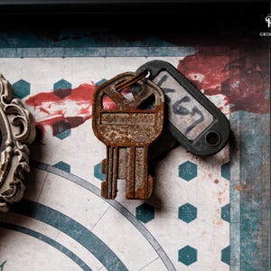 May include: A close-up of a vintage-style key with a rusty appearance, paired with a black tag labeled "K67". The key rests on a patterned background with a clock design and red accents. A decorative frame with an angel is visible.