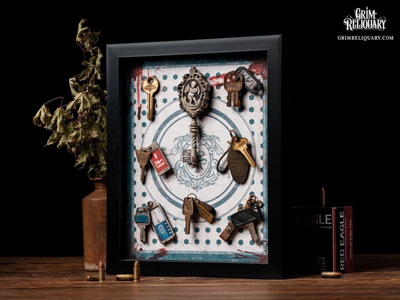 May include: A framed display featuring antique keys of various shapes and sizes, arranged on a patterned background. The keys are in shades of gold, silver, and bronze. The frame is black, and the text "Grim Reliquary" is visible.